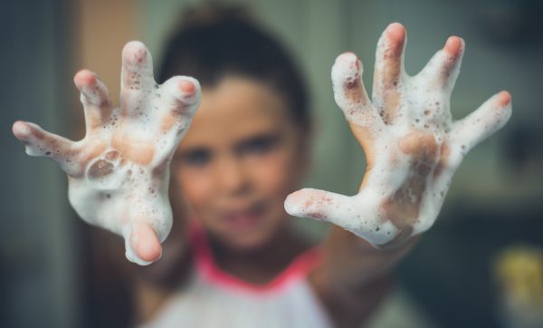 A little girl with foamy soap suds on her hands, reaching out toward the camera