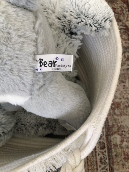 A Bear Factory tag on a gray plush animal in a basket