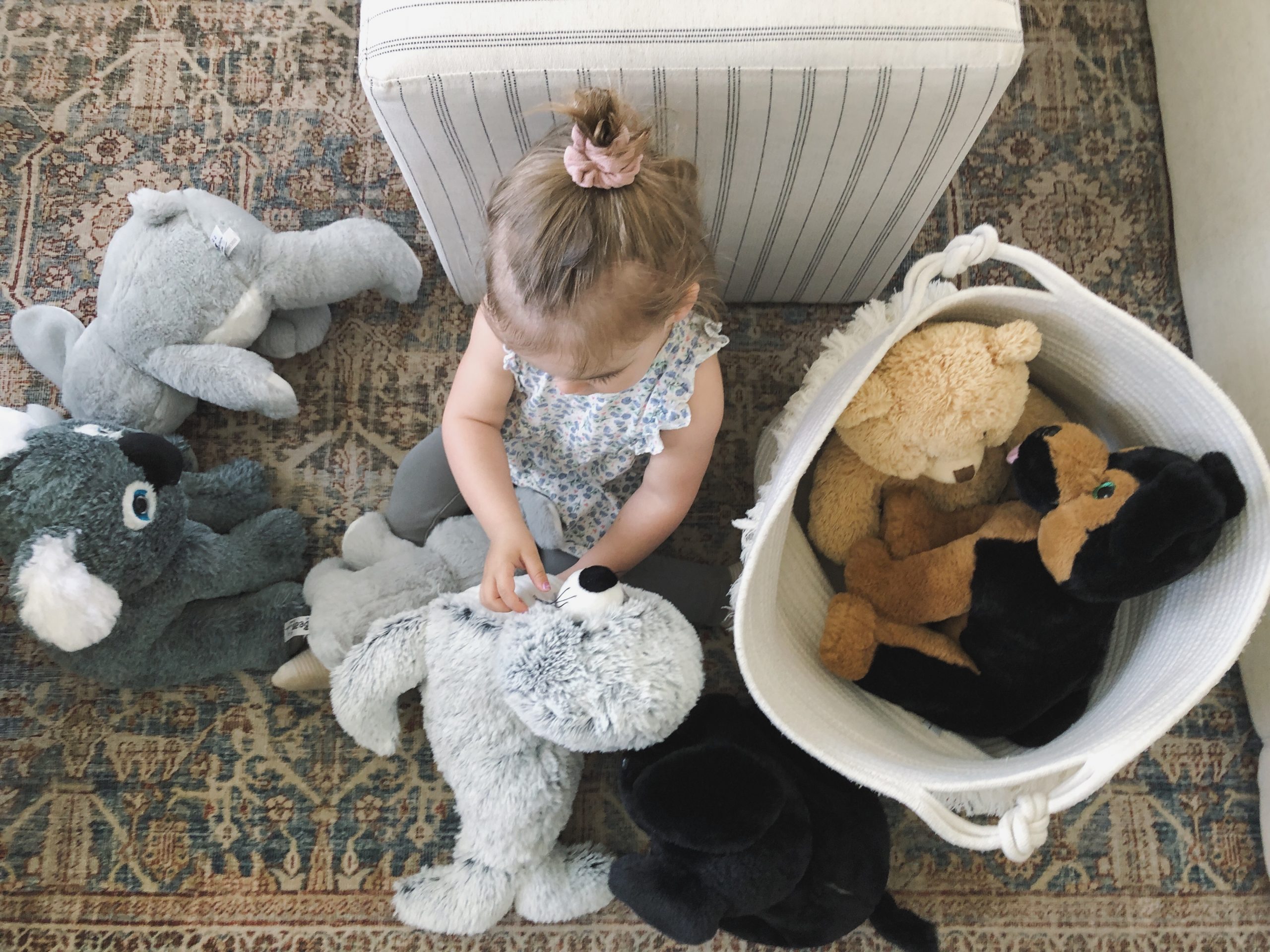Child sitting on floor surrounding by plush animal toys. Check out careers with The Bear Factory.