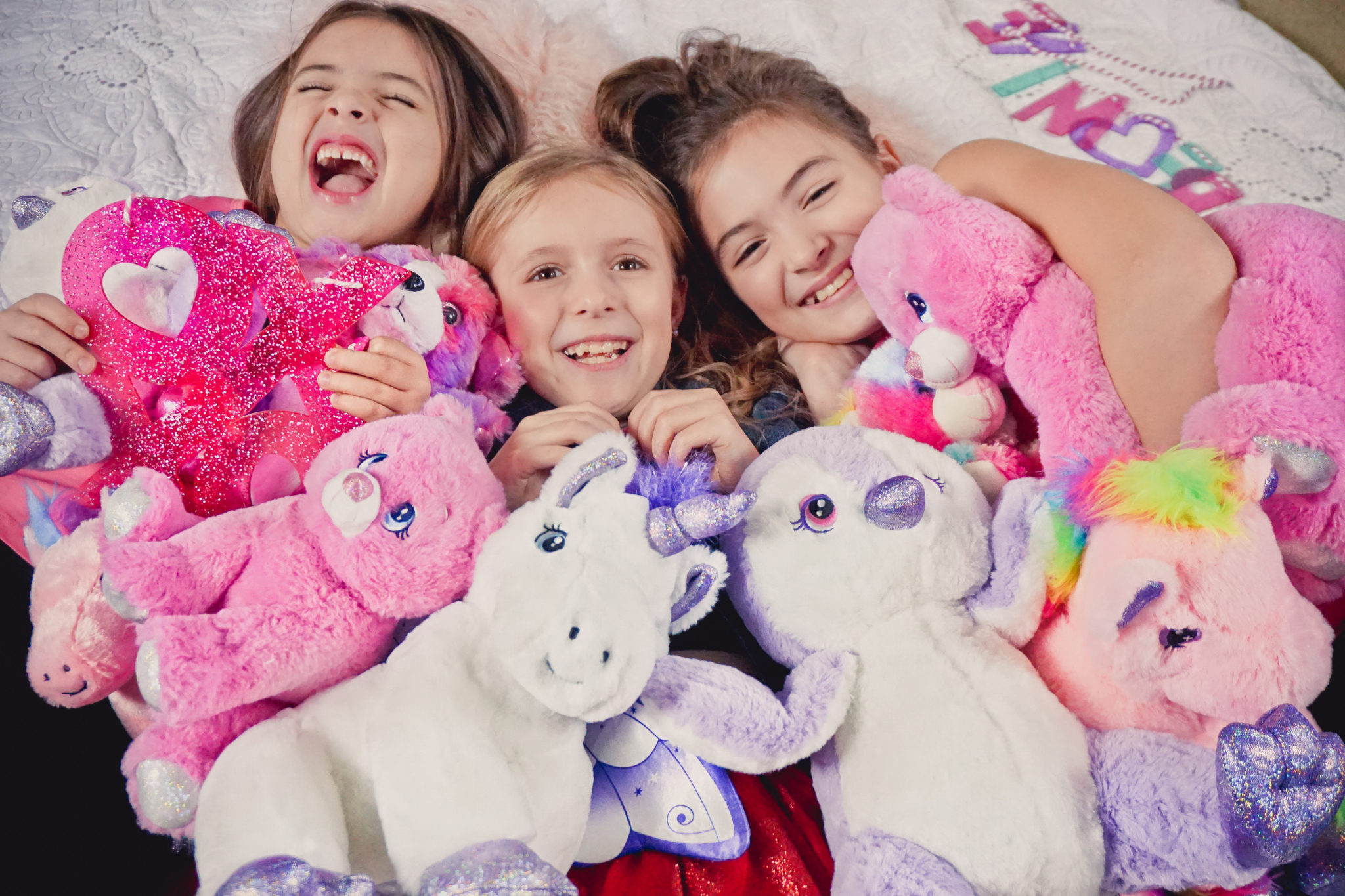 Three girls hugging stuffed plush animals in various pink and purple shades